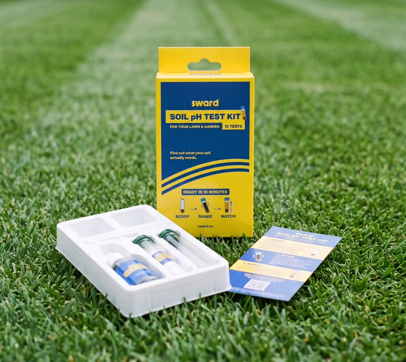 The Soil pH Test Kit box standing on a striped lawn, its open tray holding the test solution bottle and test tubes, and the colour chart card beside it.